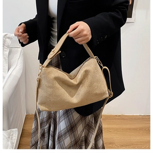 Modella tiene una borsa a tracolla in camoscio beige con dettagli dorati in un interno luminoso