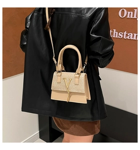 Detail of beige tote bag with gold V-shaped buckle and elegant tassel on black leather outfit