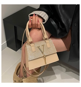 Detail of light beige crossbody bag with sparkling rhinestones and a gold V tassel charm