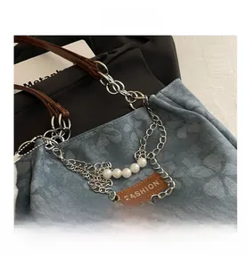 Dettaglio della borsa in denim azzurro con rilievi floreali, manico in pelle e perle