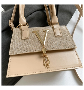 Detailed macro view of beige leather handbag featuring a gold sequined flap and V logo