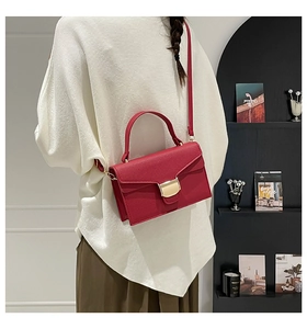 Sac à main rouge en cuir grainé avec fermoir doré porté par un mannequin en intérieur