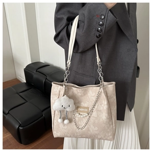 Close-up of beige canvas tote with fashion tag, pearl chain, and cloud charm
