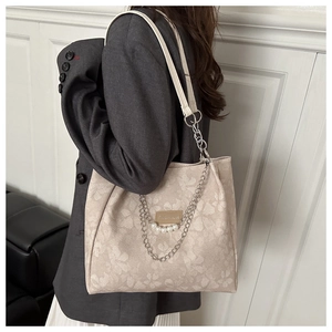 Detail of beige jacquard tote bag with floral texture, metal chain, and pearl accents
