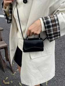 Chic black mini crossbody bag with wavy flap detail shown on stylish beige coat