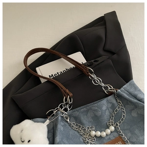 Detail of blue floral tote with pearl chain strap and cloud plush charm on black suit