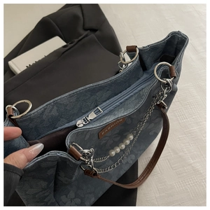 Detail of blue floral denim tote bag with chain, pearl charm, and zipper closure.