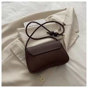 Detail of minimalist dark brown matte leather handbag with knot strap and gold metal hardware