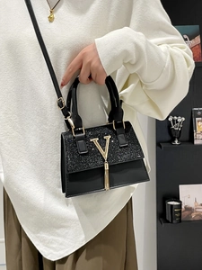 Elegant black leather handbag with glitter panel and gold V-shaped buckle on model