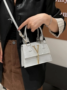 Silver mini crossbody bag with sparkly texture, gold V-logo, and round handle on model