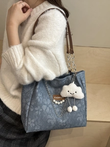 Blue denim tote bag with floral patterns and plush cloud charm worn by a model