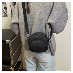 Detail of black nylon crossbody bag with adjustable strap worn by model on casual outfit