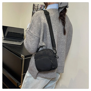 Side view of black nylon crossbody bag with adjustable strap on a model in an office