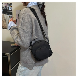 Detail of a black nylon crossbody bag with adjustable wide strap and zippered pocket