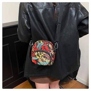 Close-up of lightweight crossbody bag with colorful tropical leaf pattern on black jacket
