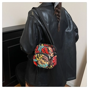 Detail of colorful tropical leaf print on small nylon crossbody bag worn with leather jacket