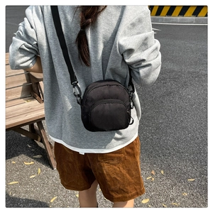 Outdoor street style shot of a versatile black crossbody bag with multiple zip pockets
