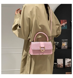 Detail of pink glitter flap crossbody bag with gold U-shaped lock on a khaki trench coat
