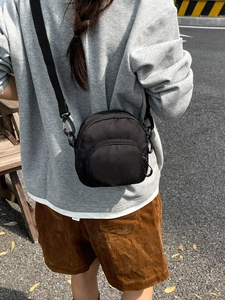 Minimalist black nylon crossbody bag with adjustable strap worn on person outdoors