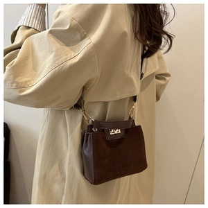 Detail of a dark brown suede crossbody bag with gold buckle on a beige trench coat