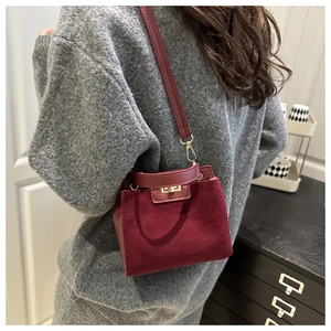 Close-up of burgundy suede Kelly bag with gold hardware worn by a model in a minimal room
