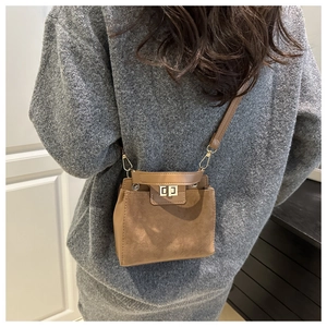 Detail of a brown leather crossbody bag with a gold metal lock and textured suede panels