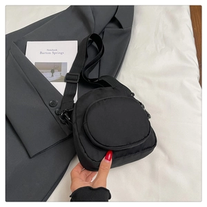 Close-up of black nylon mini crossbody bag with round front pocket and adjustable strap