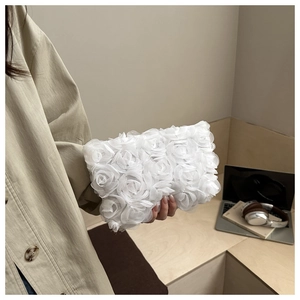 Detail of elegant white 3D fabric rose flower clutch bag held by a model in a cozy setting