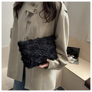 Detail of 3D rose floral evening clutch bag in black mesh held against a beige coat