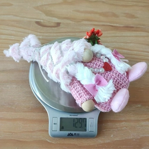 Poupée gnome en peluche rose pesant 129,7 g sur une balance montrant son poids léger