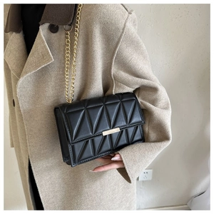 Close-up of black quilted crossbody bag with gold chain strap on a wool coat