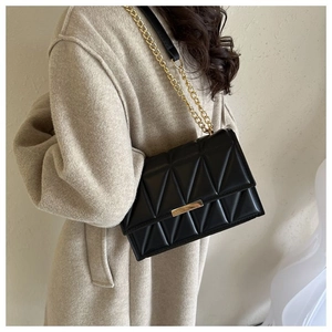 Detail of black quilted chain bag on beige wool coat showing triangular stitching