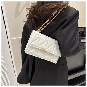 Close-up of white quilted crossbody bag with gold metal clasp and chain strap on blazer