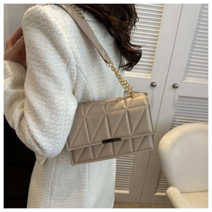 Close-up of beige quilted crossbody bag with gold chain strap worn on a white coat