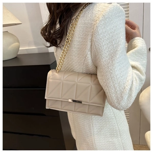 Detail of light beige quilted crossbody bag with golden chain strap on a model