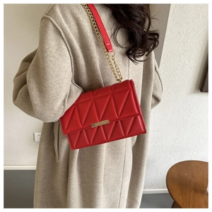 Red quilted crossbody bag with gold chain strap shown against a beige wool coat