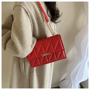 Close-up of red quilted shoulder bag with gold metal lock and chain strap on a coat
