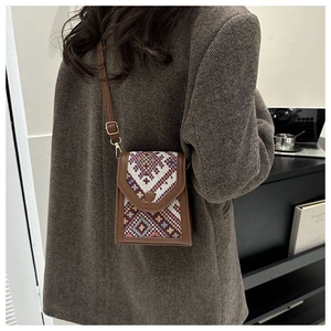 Ethnic style crossbody phone bag with geometric weaving and brown leather trim on a model