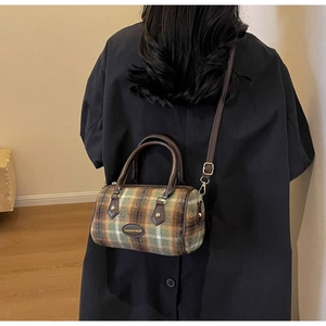 Close-up of a plaid wool Boston bag with brown leather straps worn by a model