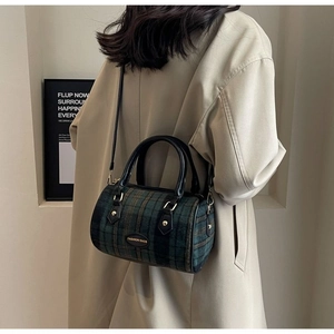 Detail of green plaid wool Boston bag with leather handles shown on a model's shoulder