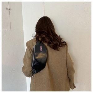 Détail d'un sac banane noir brillant avec écriture rose sur un manteau en tweed marron