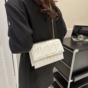 Chic white quilted crossbody bag with gold chain strap worn over a black blazer
