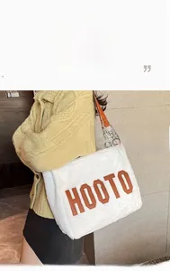 Detail of white plush tote bag featuring brown HOOTO letter embroidery and faux fur texture