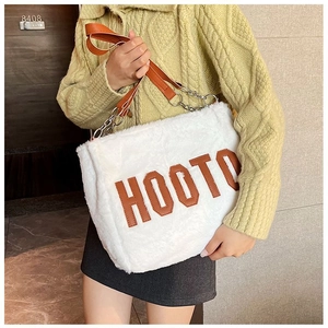 Detail of white plush tote bag with brown leather HOOTO logo and metal chain strap