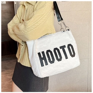 Detail of white plush tote bag featuring black lettering and metal chain strap accents