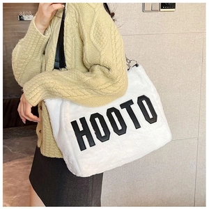 Detail of white plush tote bag showing HOOTO letter embroidery and black leather straps