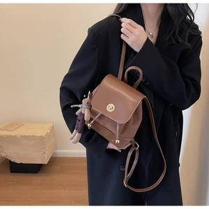 Brown leather retro backpack with gold clasp and bear charm shown on a female model