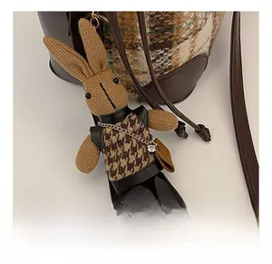 Close-up of a brown knitted rabbit bag charm with houndstooth vest and golden chain