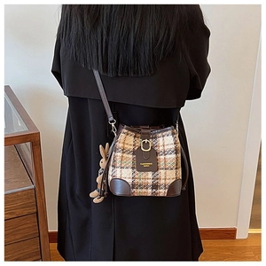 Detail of checkered tweed bucket bag featuring brown leather trim and a cute rabbit charm
