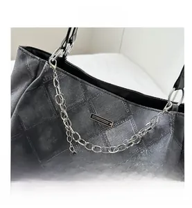 Macro view of grey quilted denim tote bag featuring vintage metal chain and logo detail